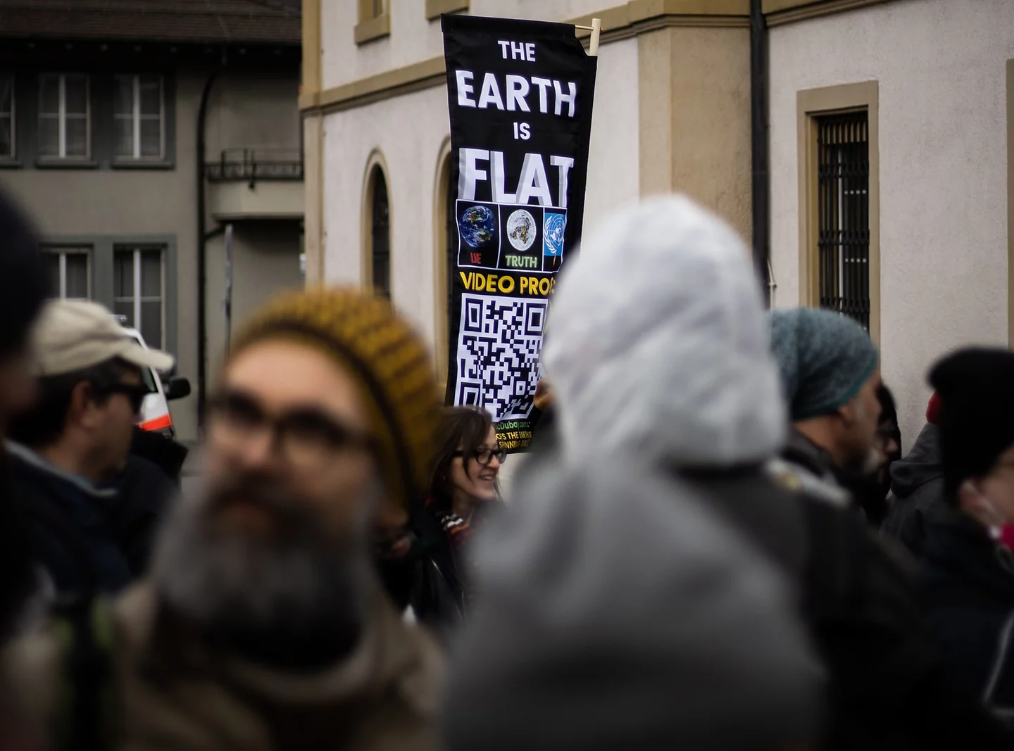 A busy street with a sign hanging that says "The earth is flat"